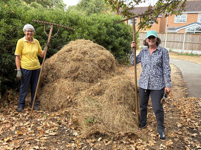 Two volunteers standing beside the final haystack of cut vegetation.